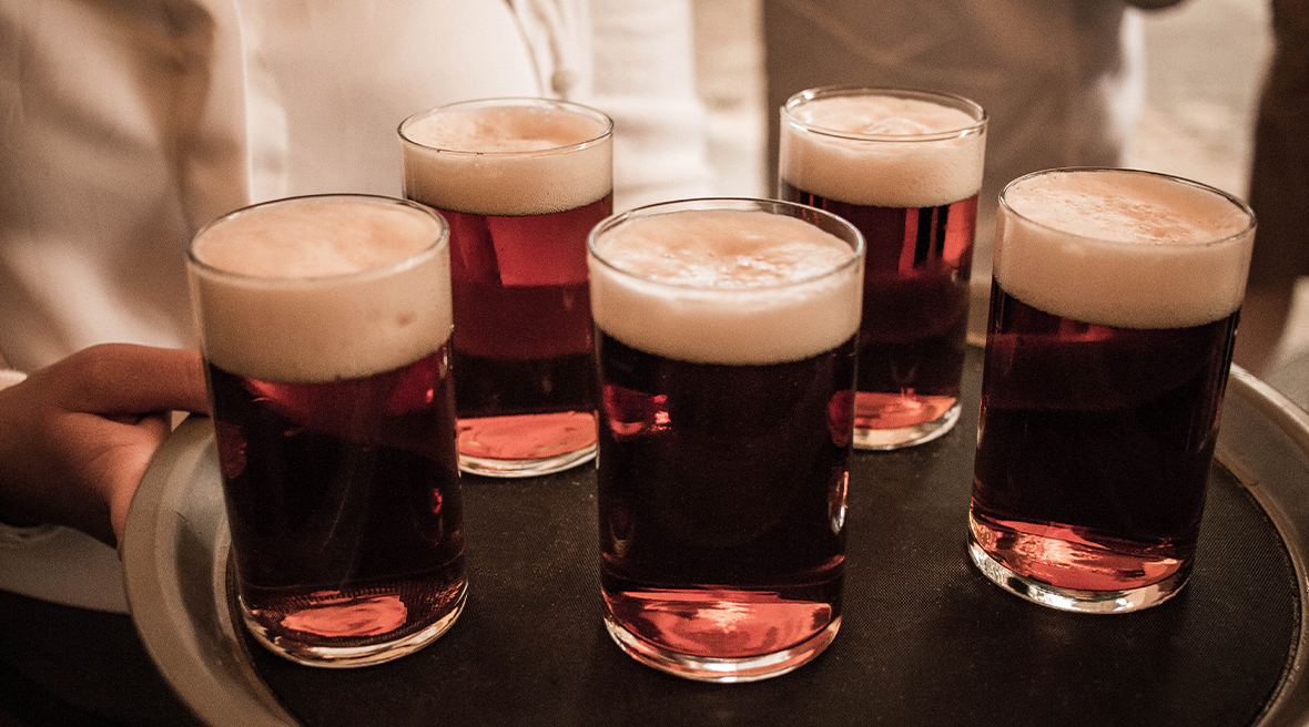Five glasses of dark beer on a tray being held by a waiter