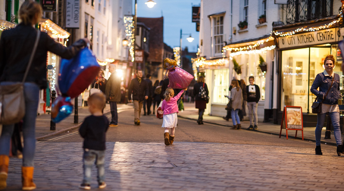 children carrying balloons on the Streets of Canterbury lit up with Christmas lights