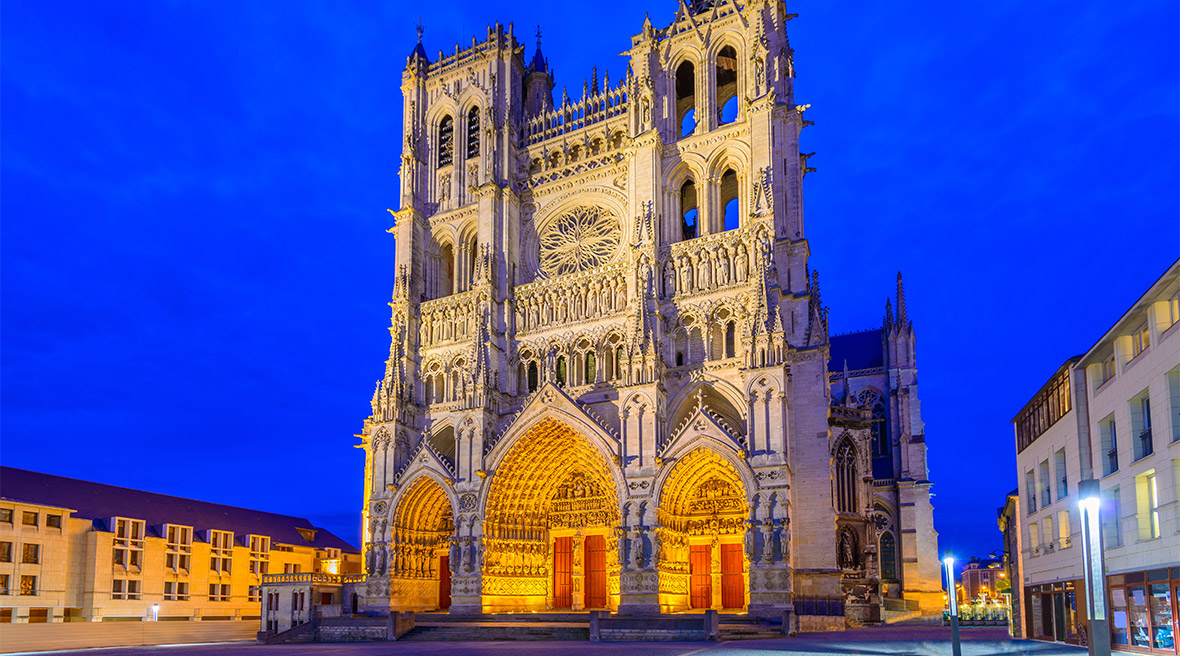 Cathédrale Notre-Dame d'Amiens at night with entrance way lit up. 13th-century Gothic edifice, famous for lavish decoration & carvings, with 2 unequal towers.