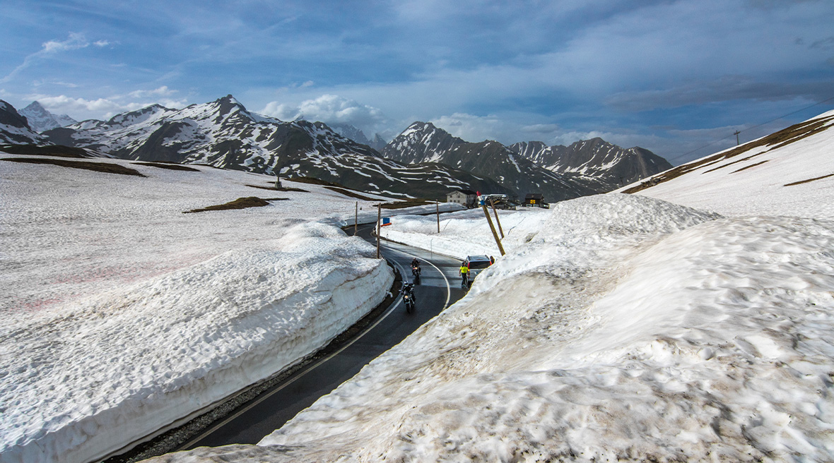 snowy roadside with cars and motorbikes driving along the Petit St Bernard Pass
