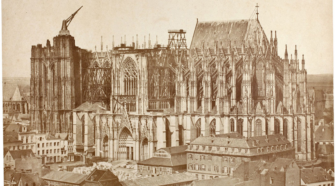Sepia photograph of a cathedral under construction in the heart of a city.