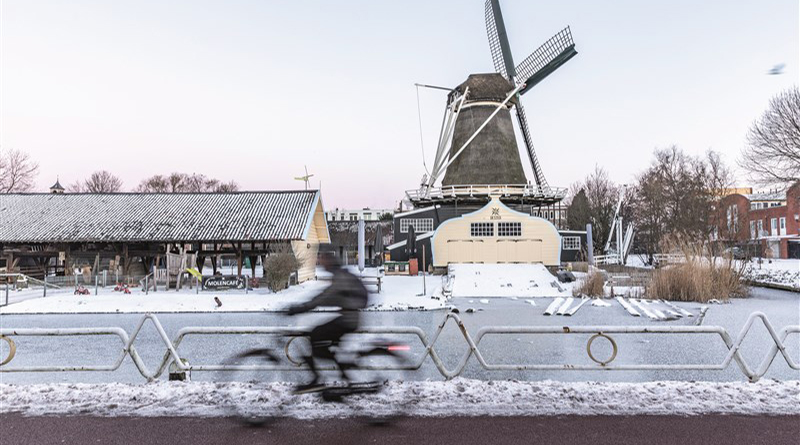 A cyclist skirts the canal in Utrecht where a windmill graces the winter city skyline