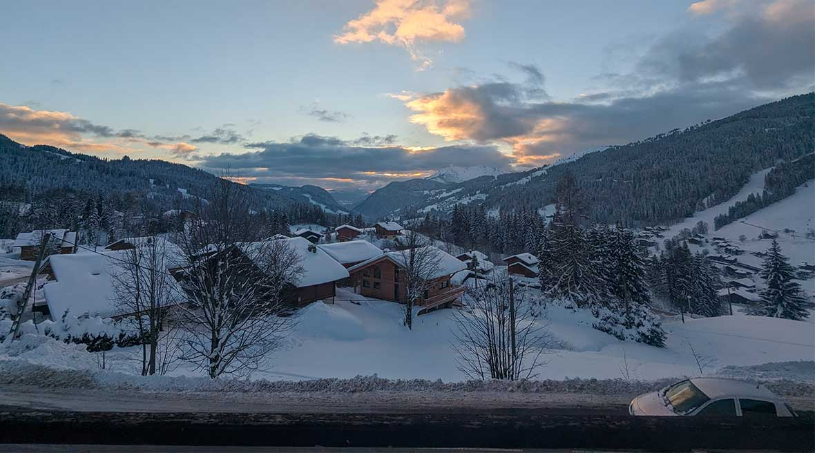 A view of sunset down the valley over snowy wooden chalets and with mountains on either side