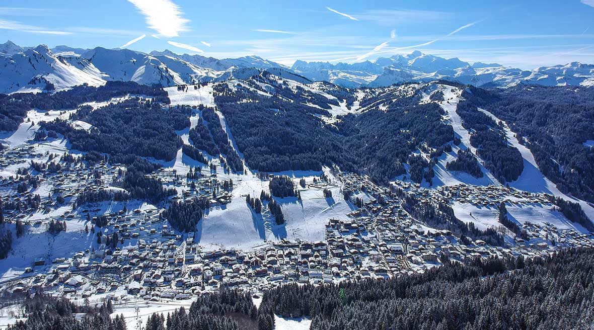 Looking down on hundreds of snowy roofs in the valley and across the valley to the snowy tree-lined pistes