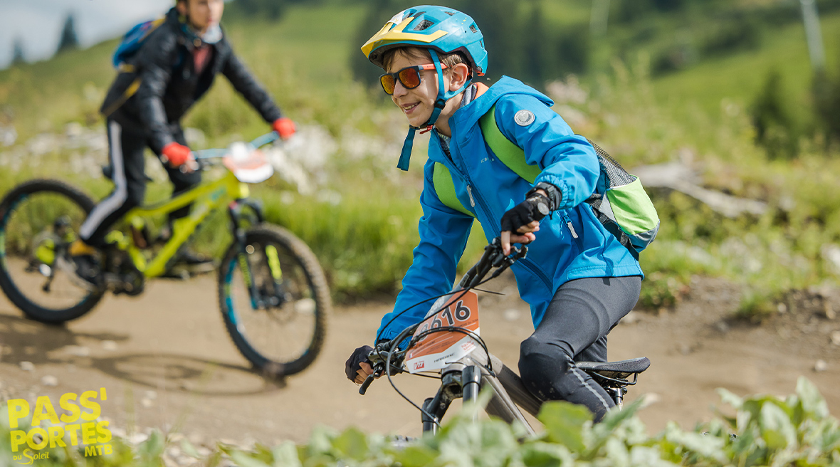 A young child in helmet, sunglasses and jacket rides his bike along a mountain path in summer