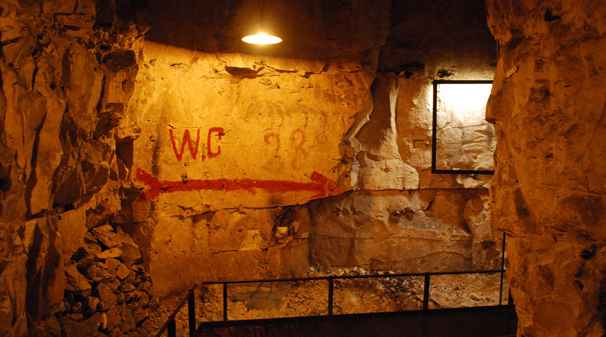 Red arrow, letters and numbers drawn on an underground cave wall, with a walkway and electric lights