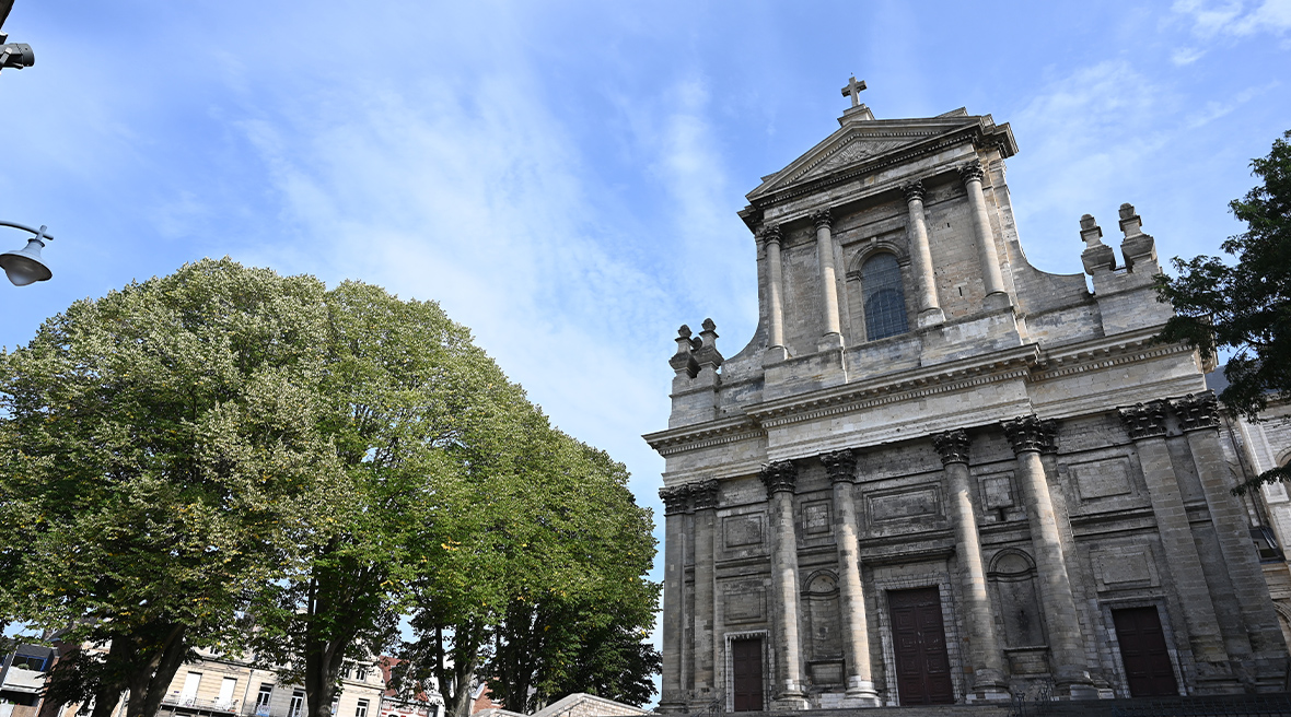 A stone neo-classical church with trees to the left of it and a clear blue sky behind it