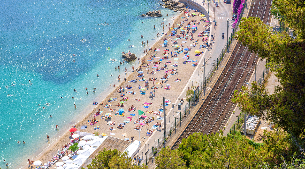 People sunbathing on Villefranche-sur-Mer beach with the railway track running along the right side of the image