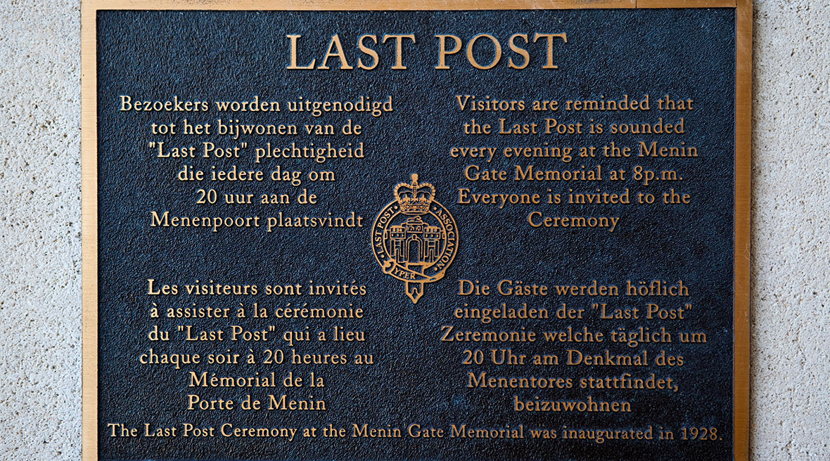 Plaque on a wall in four different languages about the Last Post ceremony at the Menin Gate