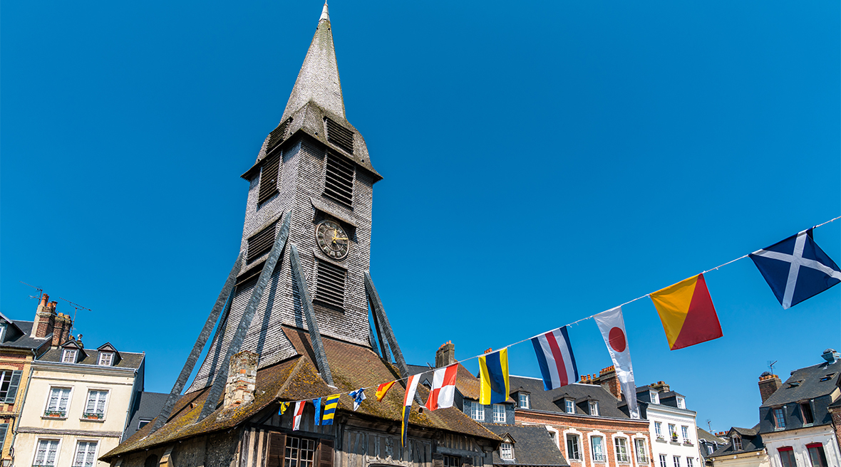 A bell tower and clock supported by a wooden building in a town square on a summer’s day