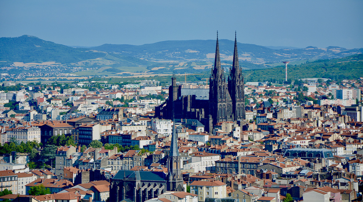 A Gothic cathedral with two spires stands out amidst lower buildings of a lighter colour of a cityscape