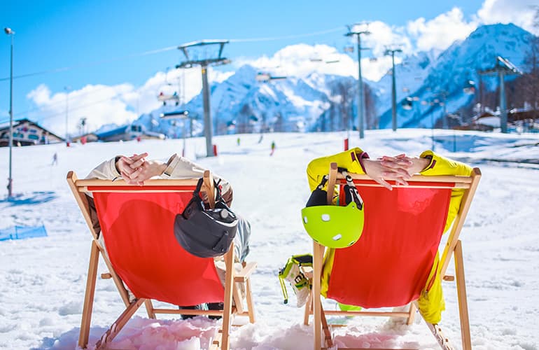 Couple sitting in deck chairs watching skiers descending the mountain