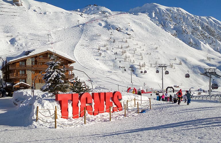 Ski station of Tignes in winter, with letters Tignes and people walking `