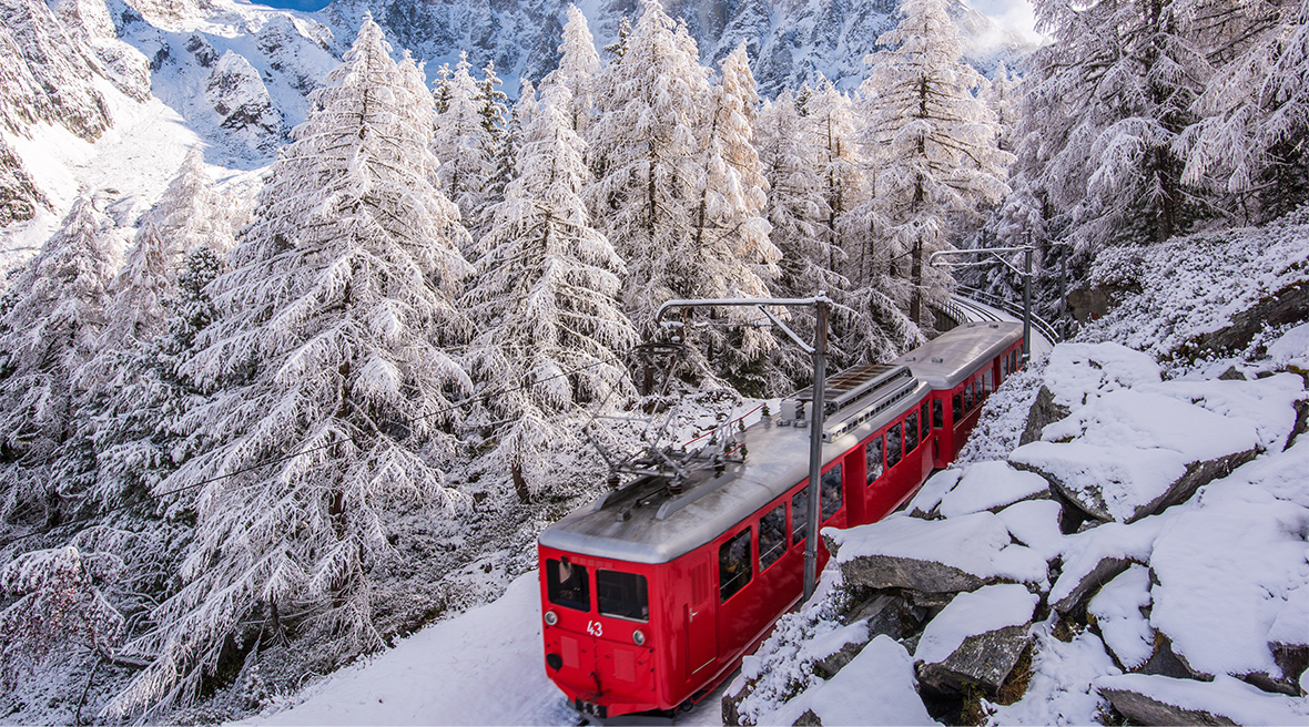 A red two carriage train chugs through a snowy landscape on a beautiful winter’s day