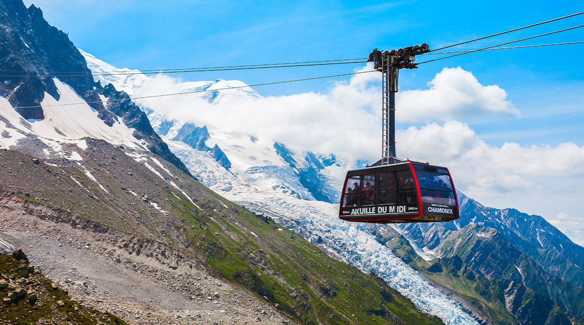 A carriage of a cable car travelling at altitude amongst a high range of cloud and snow-capped peaks