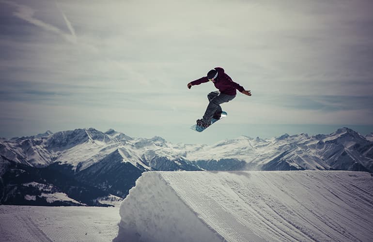 Snowboarder going over a jump with snow covered mountains in the background