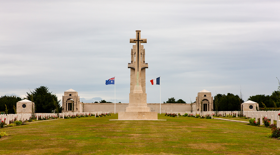 A monumental stone cross flanked by the flags of Australia and France with military gravestones either side