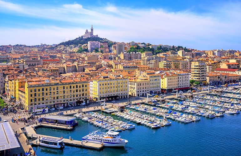 A panoramic view of a big colourful city with a harbour filled with boats on blue water