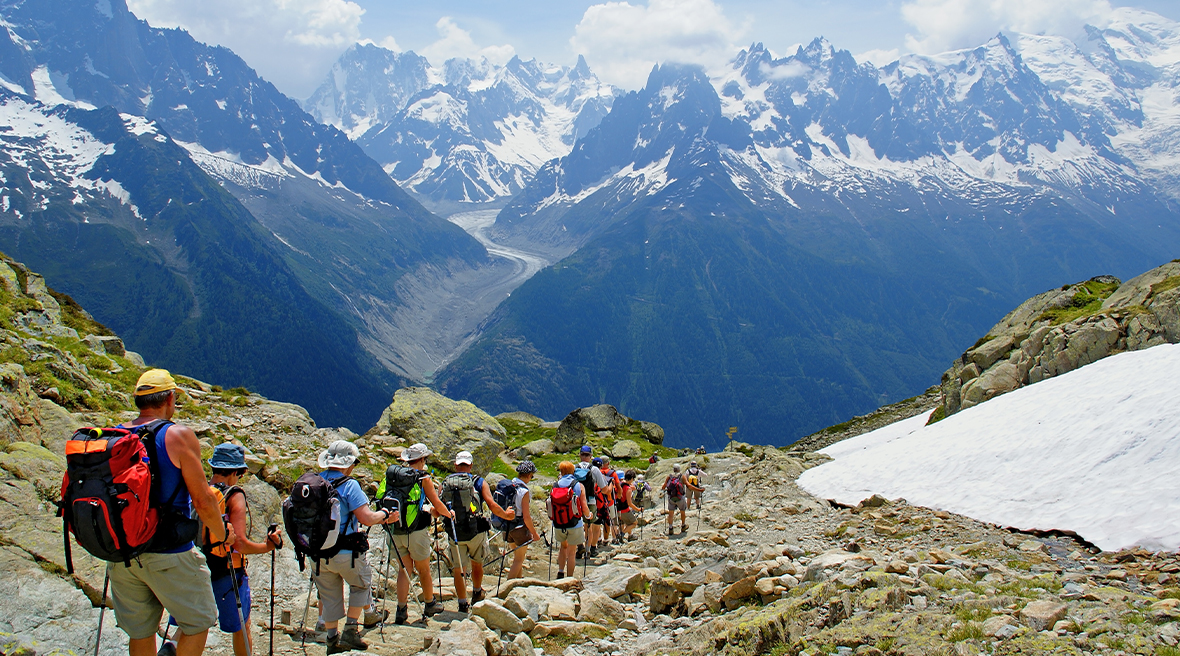 Hikers in a group walking down a high pass with spectacular snow-capped peaks in the distance.